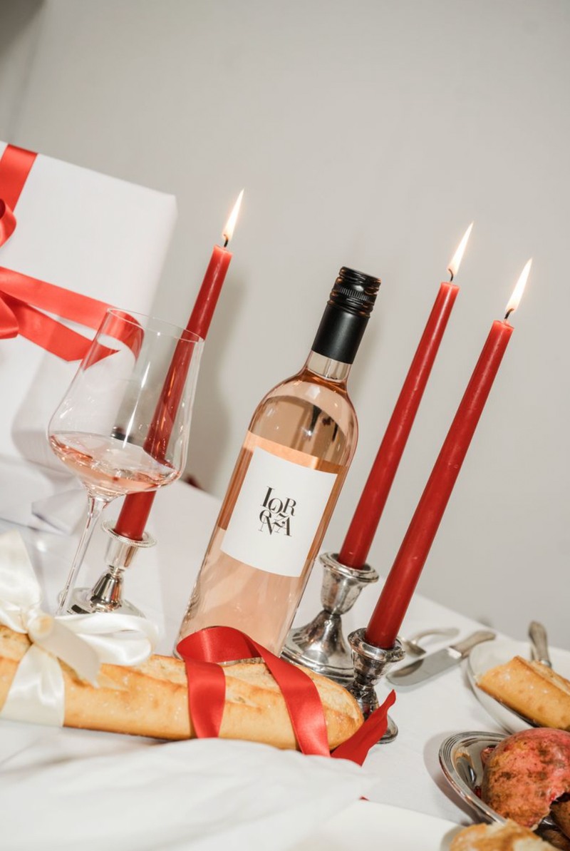 Bottle of Lorenza Rosé, glass, bread, and candles on a table with a white background